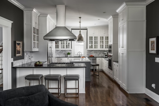 kitchen with a peninsula, a breakfast bar, appliances with stainless steel finishes, island exhaust hood, and glass insert cabinets