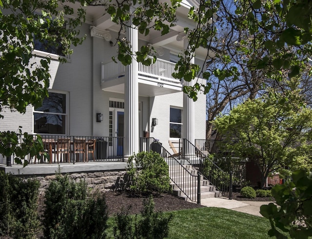 view of exterior entry with a balcony, a porch, and brick siding