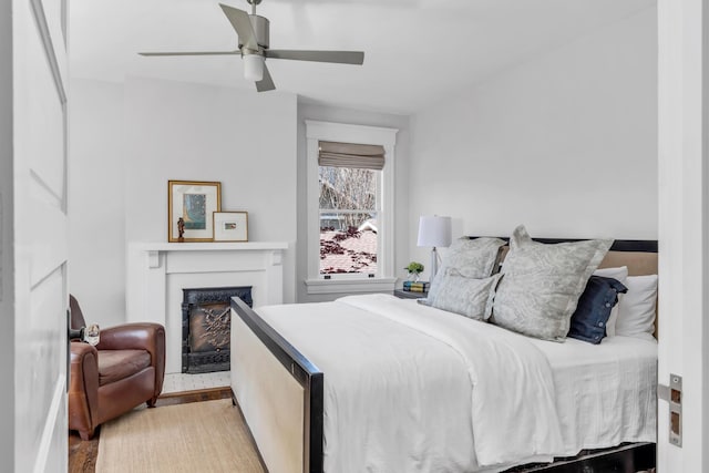 bedroom with ceiling fan, a fireplace, and wood finished floors