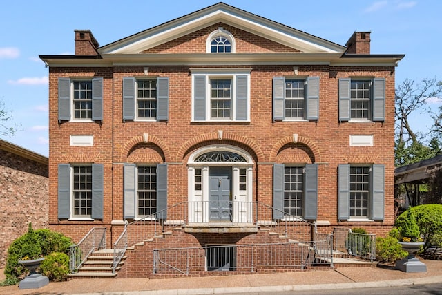 georgian-style home featuring a fenced front yard, a chimney, and brick siding