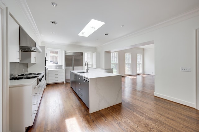 kitchen featuring stainless steel appliances, wall chimney range hood, an island with sink, and crown molding