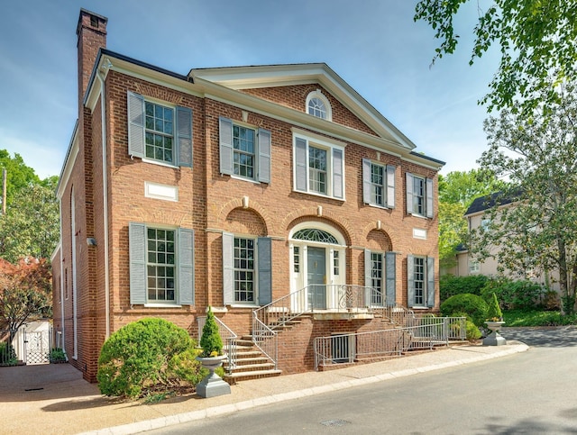 view of front of house featuring brick siding, fence, and a chimney