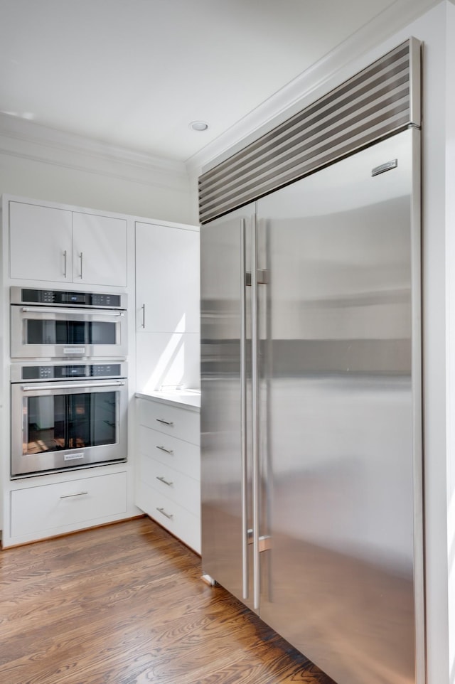 kitchen featuring white cabinetry, stainless steel appliances, crown molding, and wood finished floors