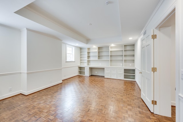 unfurnished room featuring built in features, a raised ceiling, ornamental molding, built in study area, and baseboards