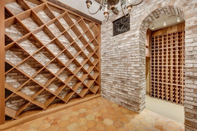 wine cellar with a notable chandelier, brick wall, and track lighting