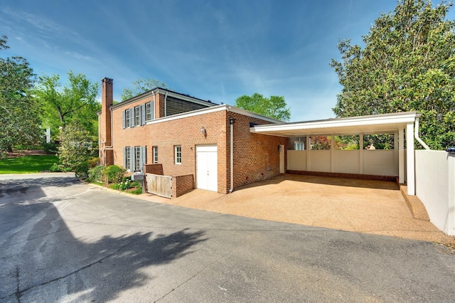 view of side of home featuring brick siding, a chimney, fence, a carport, and driveway