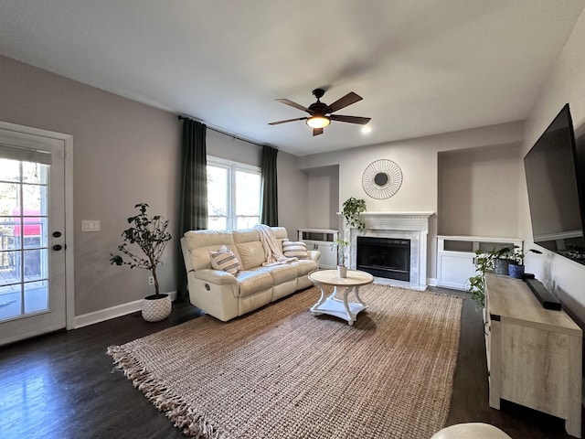 living room with ceiling fan, a premium fireplace, baseboards, and dark wood finished floors