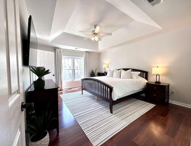 bedroom with ceiling fan, wood finished floors, visible vents, baseboards, and a tray ceiling