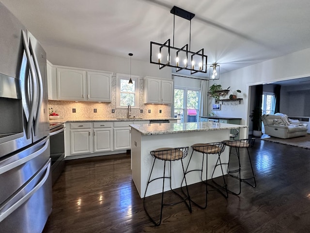 kitchen with a breakfast bar, a sink, white cabinets, tasteful backsplash, and stainless steel fridge