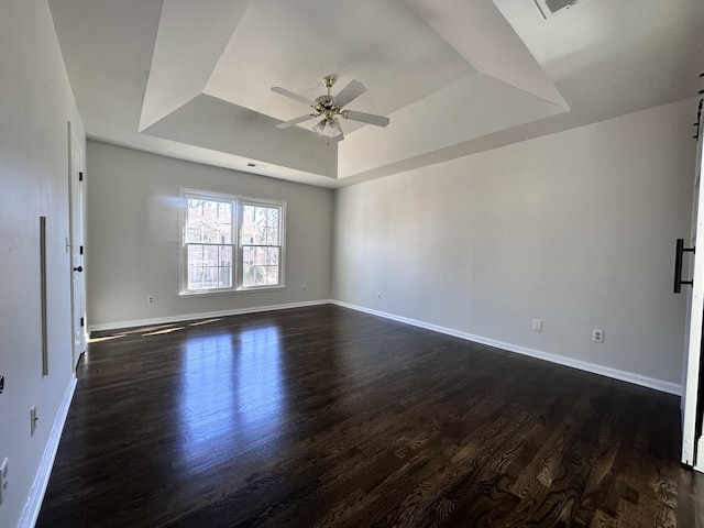 unfurnished room with a ceiling fan, baseboards, a tray ceiling, and dark wood-style flooring