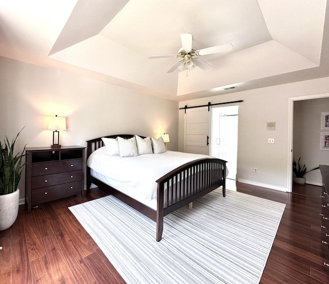 bedroom with a tray ceiling, wood finished floors, and a barn door