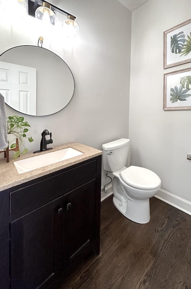 half bathroom with toilet, baseboards, wood finished floors, and vanity