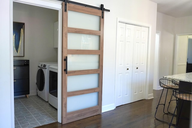 clothes washing area featuring dark wood-type flooring, washer and clothes dryer, baseboards, and a barn door