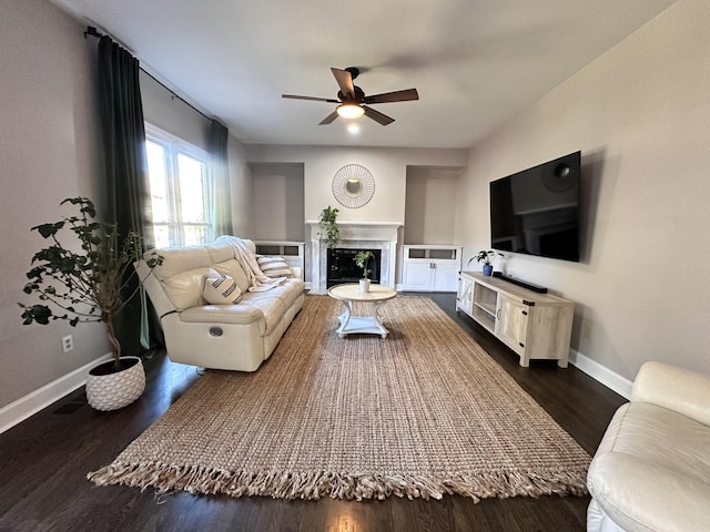 living room featuring ceiling fan, dark wood-style flooring, a glass covered fireplace, and baseboards