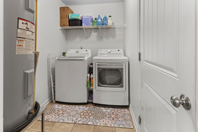 clothes washing area with laundry area, light tile patterned floors, baseboards, washer and dryer, and water heater