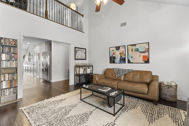 living area featuring ceiling fan, a high ceiling, wood finished floors, visible vents, and baseboards