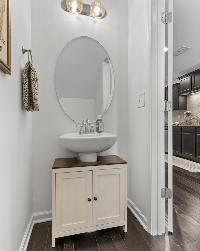 bathroom featuring baseboards, visible vents, wood finished floors, vanity, and backsplash