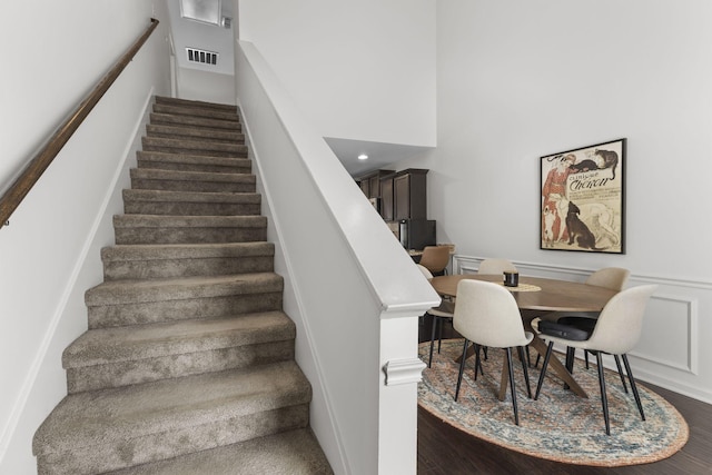 stairway with visible vents, a wainscoted wall, wood finished floors, a high ceiling, and a decorative wall