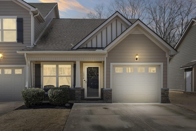 craftsman-style house featuring a garage, driveway, a shingled roof, stone siding, and a porch