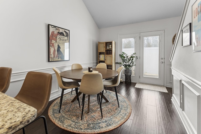 dining space with a wainscoted wall, vaulted ceiling, dark wood finished floors, and a decorative wall