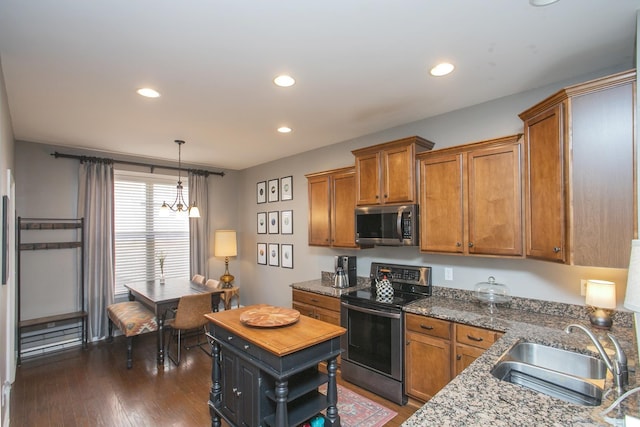 kitchen with pendant lighting, dark wood finished floors, appliances with stainless steel finishes, brown cabinetry, and a sink