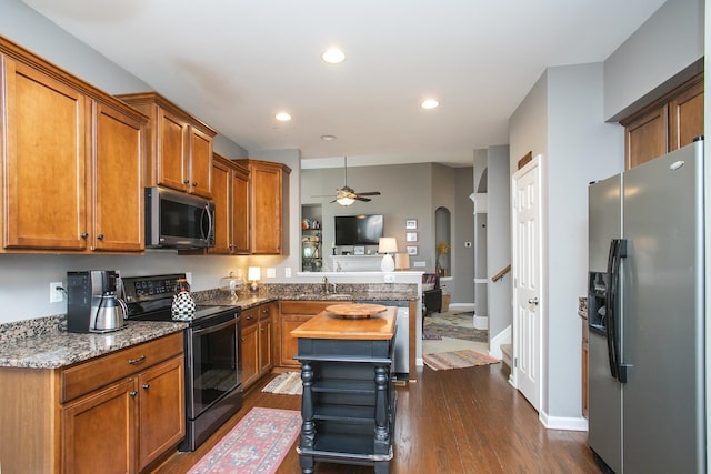 kitchen with arched walkways, brown cabinetry, dark wood-style floors, appliances with stainless steel finishes, and a peninsula