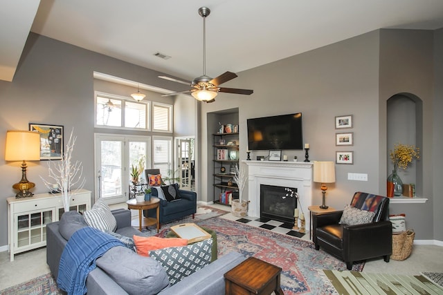 living area featuring visible vents, baseboards, a ceiling fan, a fireplace with flush hearth, and built in shelves