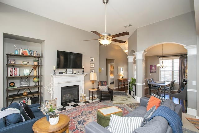 living area featuring decorative columns, visible vents, arched walkways, a fireplace with flush hearth, and ceiling fan with notable chandelier