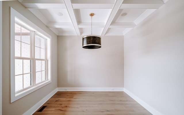 unfurnished dining area featuring baseboards, visible vents, coffered ceiling, light wood-type flooring, and beam ceiling