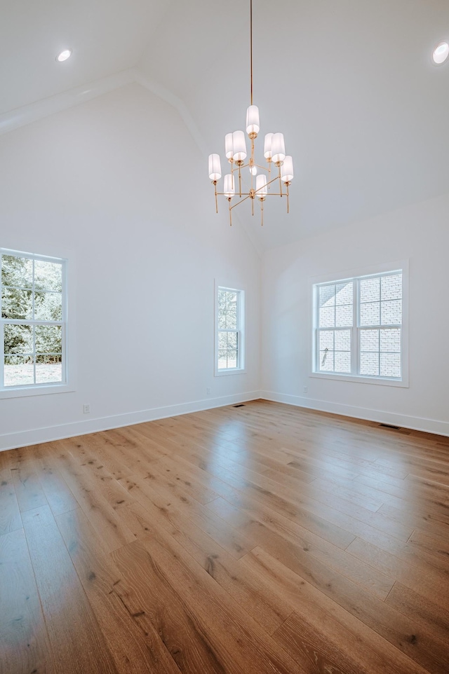 spare room with a chandelier, high vaulted ceiling, hardwood / wood-style floors, and baseboards