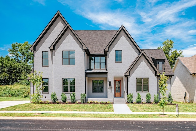 view of front facade featuring a shingled roof, brick siding, and a front lawn