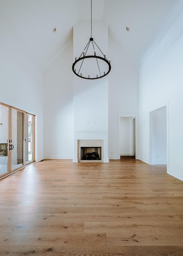 unfurnished living room with high vaulted ceiling, light wood finished floors, a fireplace, and baseboards