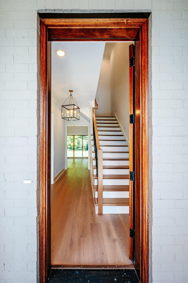 stairs with baseboards, a notable chandelier, brick wall, and wood finished floors