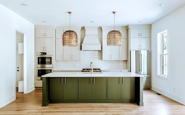 kitchen with custom exhaust hood, stainless steel appliances, light countertops, white cabinetry, and plenty of natural light