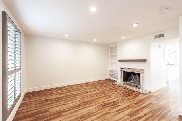 unfurnished living room with built in shelves, a fireplace, visible vents, baseboards, and light wood-style floors