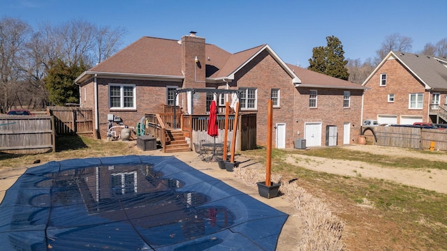 rear view of house with central air condition unit, a fenced backyard, a chimney, and brick siding