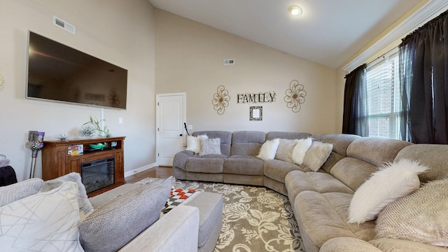 living room with lofted ceiling, wood finished floors, a glass covered fireplace, and visible vents