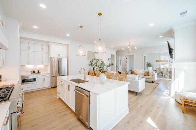 kitchen featuring stainless steel appliances, visible vents, light wood-style flooring, a kitchen island with sink, and a sink