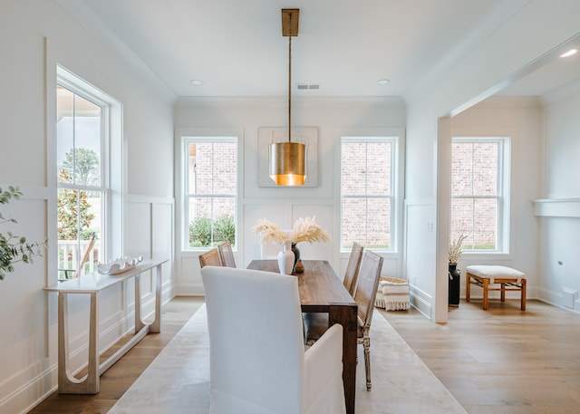 dining room with ornamental molding, light wood finished floors, a healthy amount of sunlight, and a decorative wall