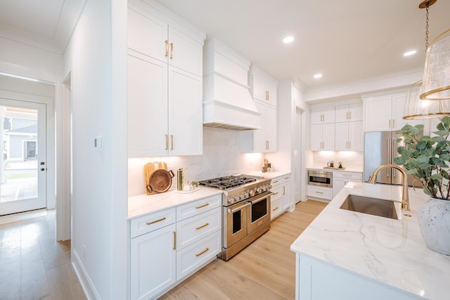 kitchen featuring premium range hood, a sink, light wood finished floors, high end appliances, and tasteful backsplash