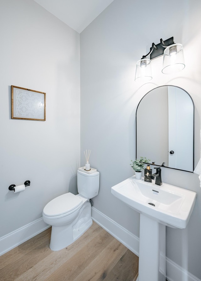 half bathroom with wood finished floors, toilet, and baseboards