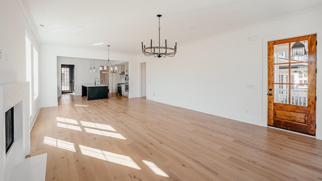 unfurnished living room featuring crown molding, an inviting chandelier, light wood-style floors, a fireplace with flush hearth, and baseboards