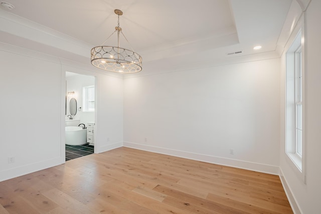 unfurnished dining area with visible vents, light wood finished floors, ornamental molding, a tray ceiling, and an inviting chandelier