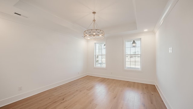 empty room with light wood-type flooring, a raised ceiling, visible vents, and baseboards