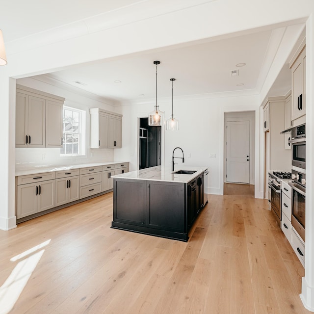 kitchen with pendant lighting, ornamental molding, light wood-style floors, a kitchen island with sink, and a sink