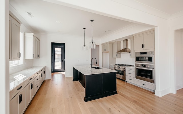 kitchen featuring light wood finished floors, wall chimney exhaust hood, light stone counters, stainless steel appliances, and crown molding