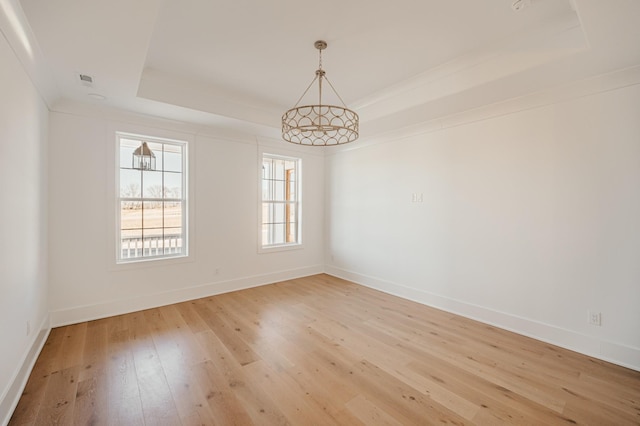 spare room featuring light wood finished floors, a tray ceiling, and baseboards