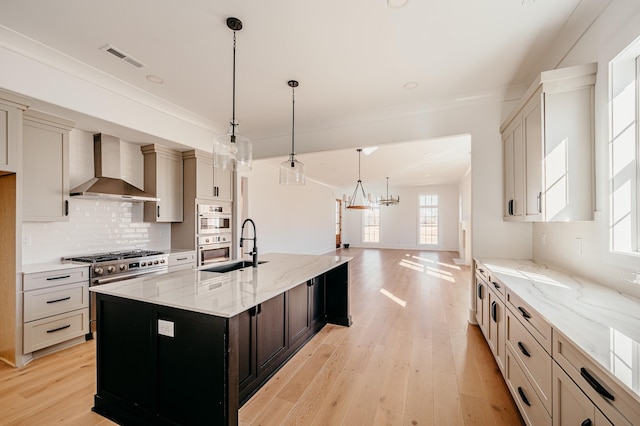 kitchen with visible vents, decorative backsplash, light wood-style flooring, light stone counters, and wall chimney range hood