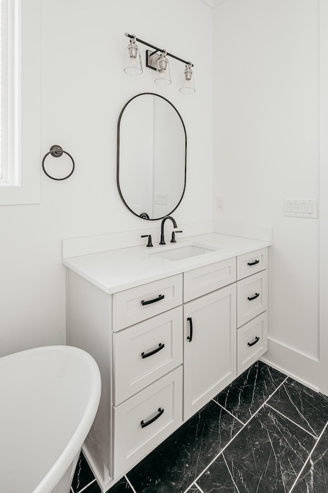 bathroom with marble finish floor, a soaking tub, vanity, and baseboards