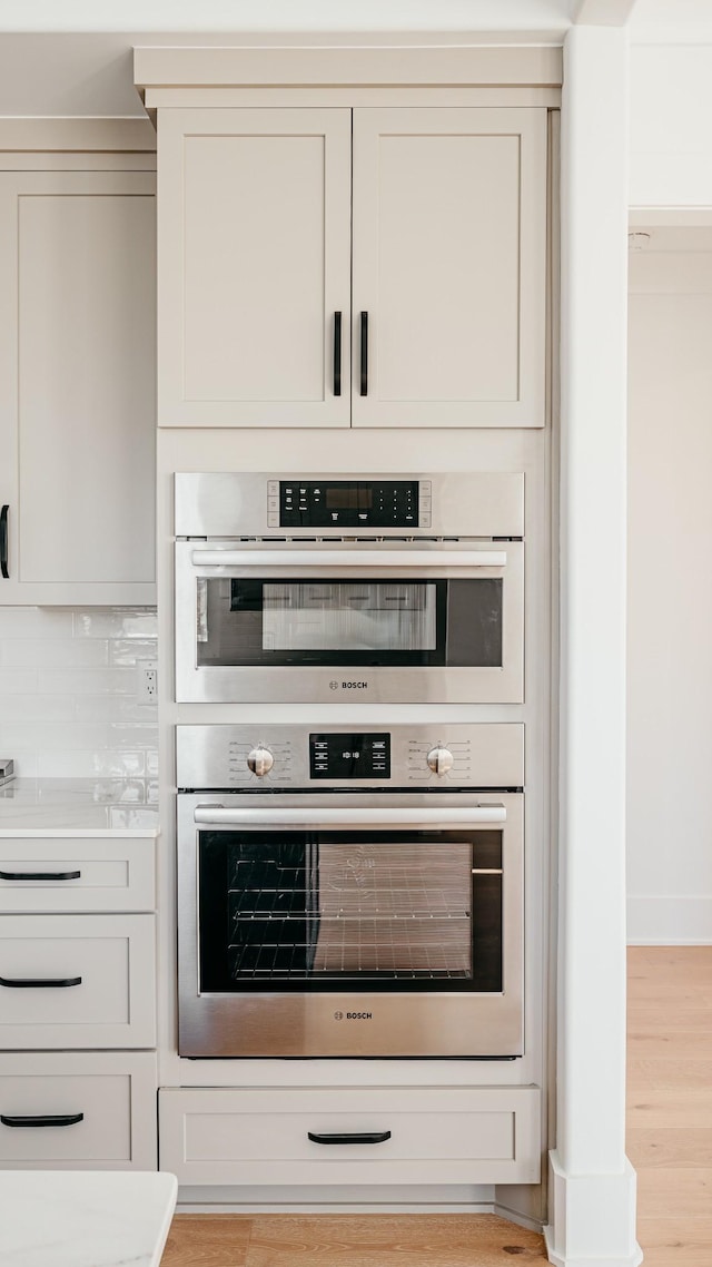 interior space with double oven, light wood-style flooring, baseboards, light countertops, and decorative backsplash